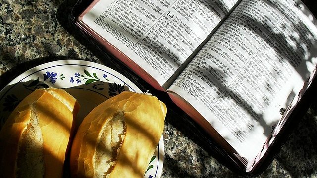 an open bible as spiritual nourishment alongside two small loaves of bread for physical nourishment