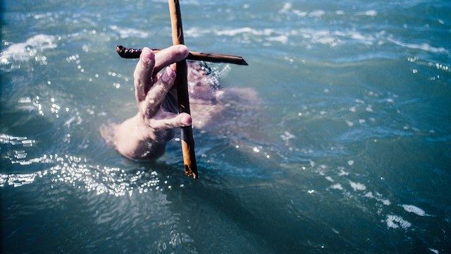 A hand emerging from the ocean holding a cross